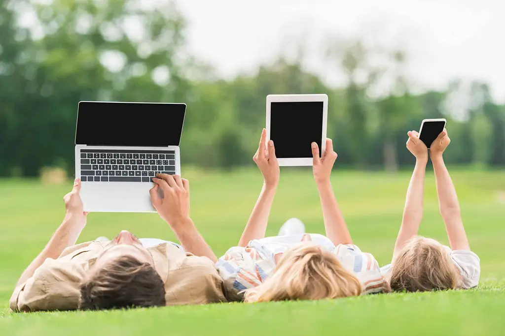 family lying on grass and using digital devices with blank screens
